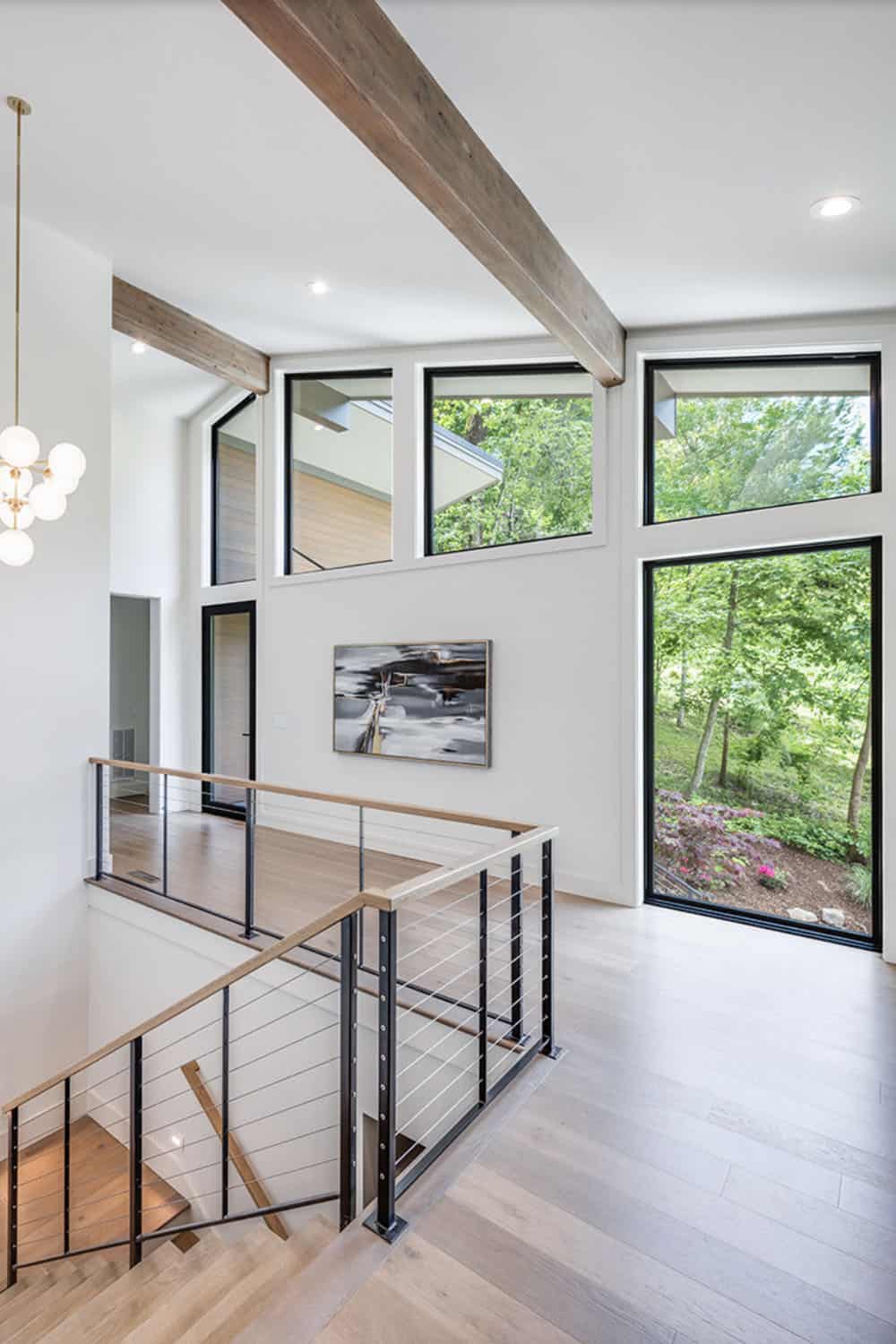 Upper-floor landing with cable railing, wood beams, and tall windows overlooking trees