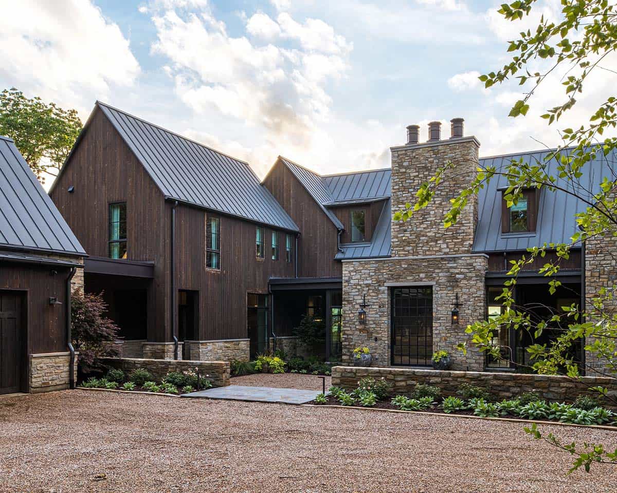 Rear courtyard view showing dark vertical wood siding, multiple gabled roof forms, and a tall stone chimney with three flues