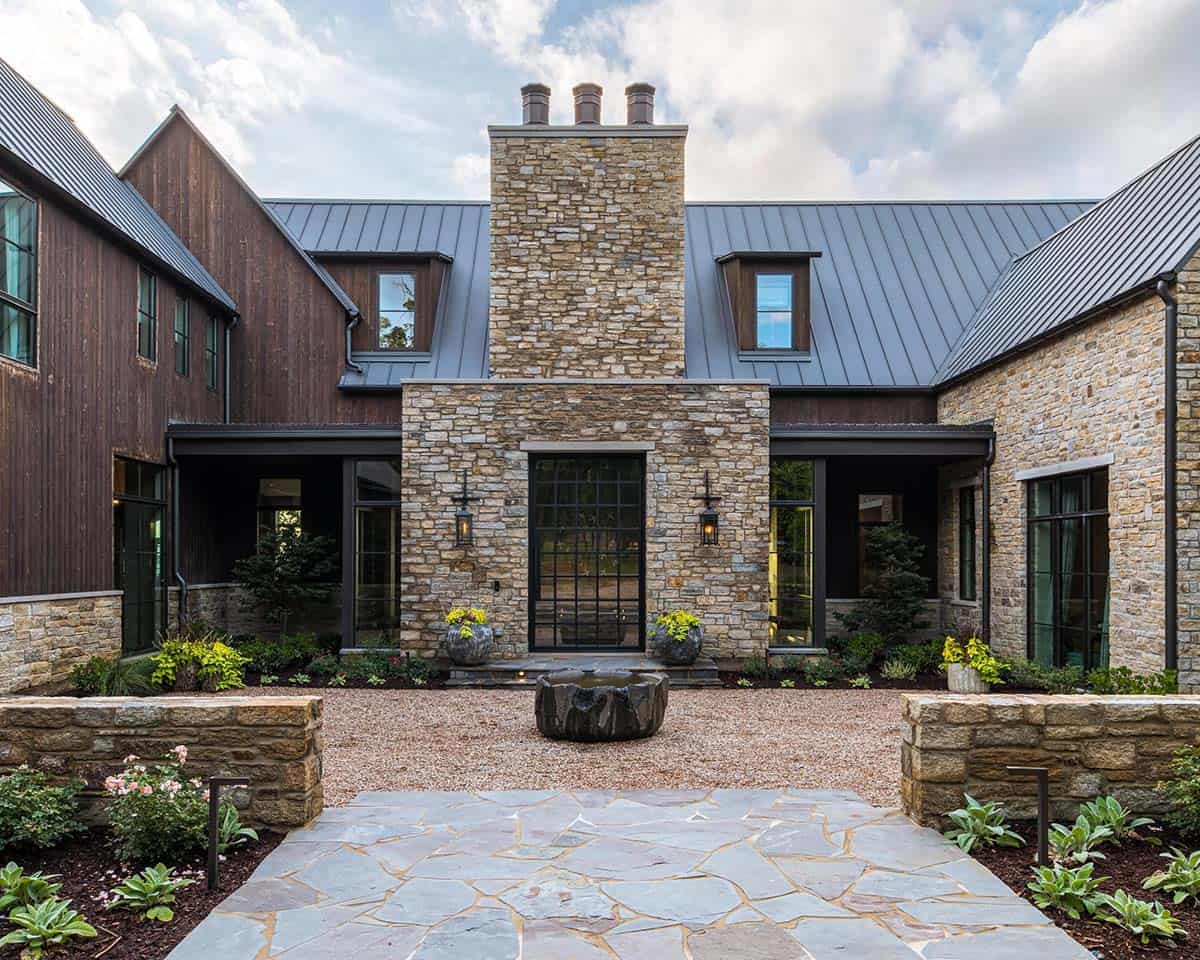 Symmetrical courtyard facade centered on a tall stone chimney with glass entry door, flanked by covered walkways and a flagstone patio