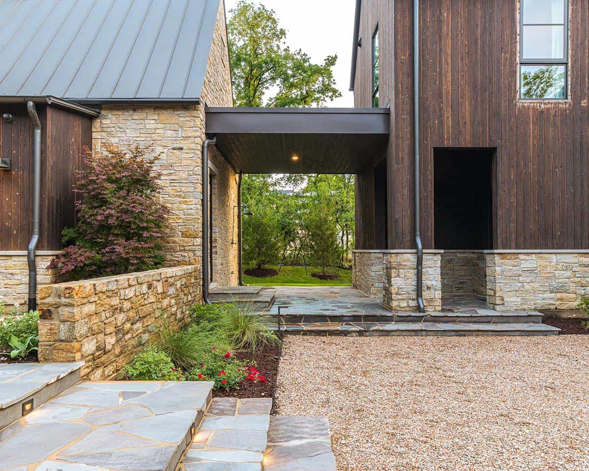 Covered breezeway connecting stone and dark wood building wings, opening to a green lawn beyond
