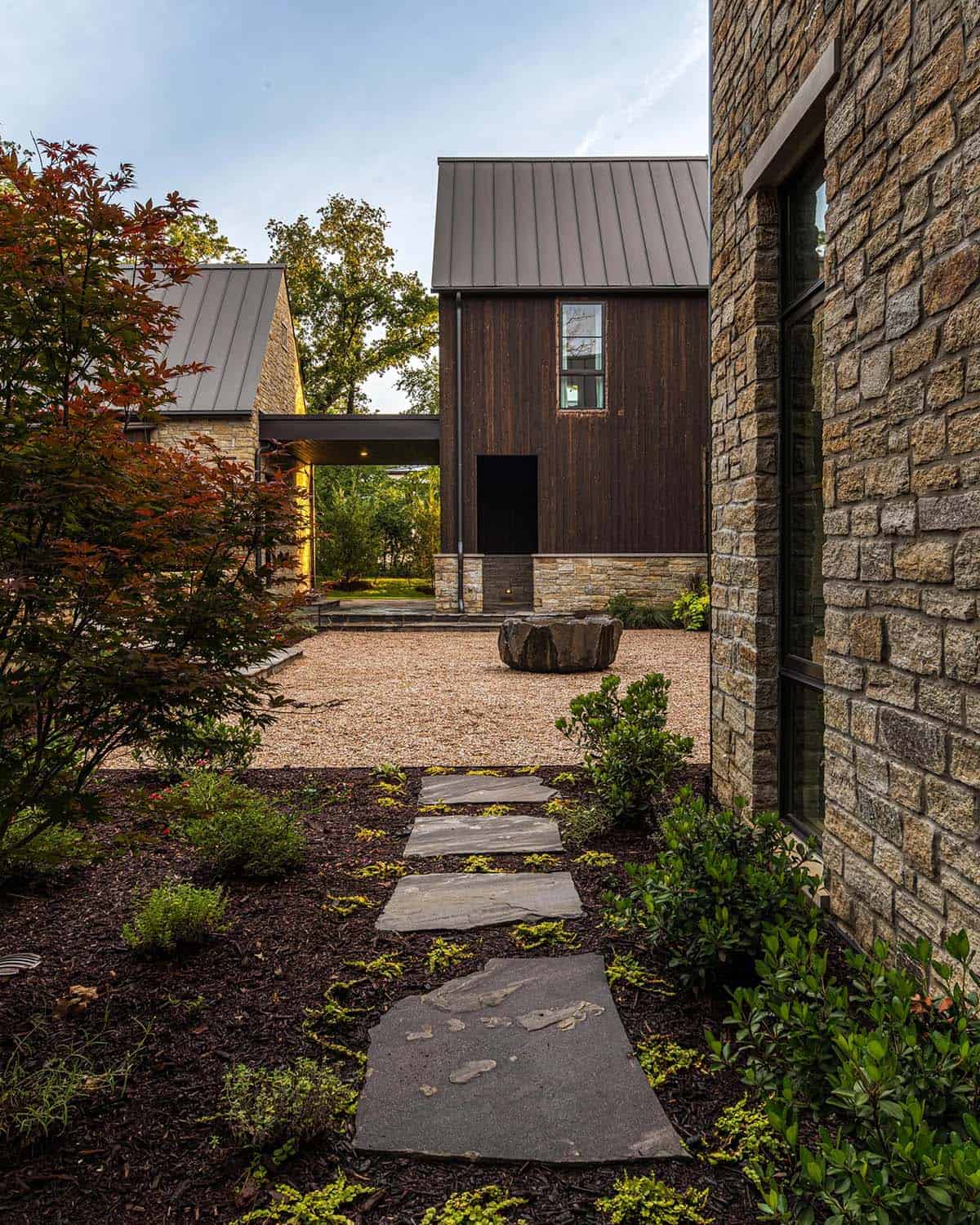 Courtyard view past a Japanese maple toward a wood-sided structure with metal roof and a sculptural stone water basin