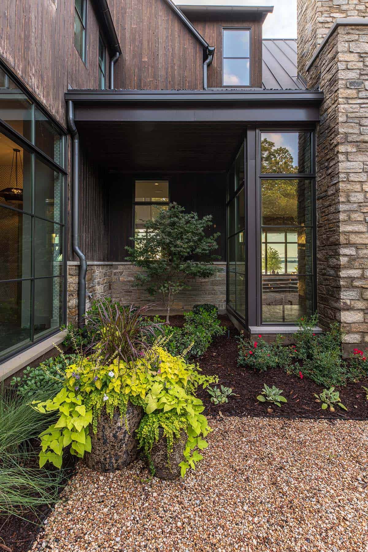 Covered glass-walled entry nook with a small Japanese maple, stone walls, and a glimpse of the lake beyond