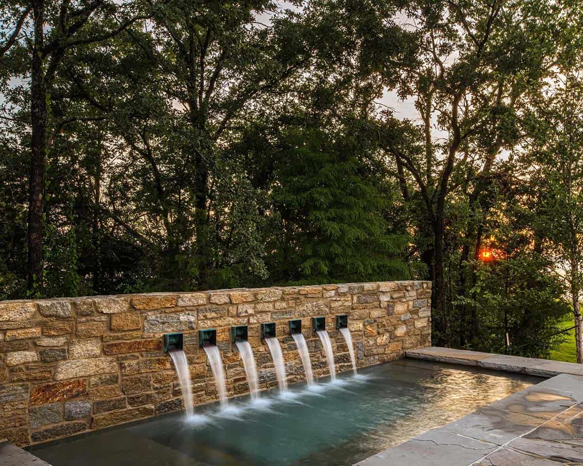 Close-up of a stone spillway wall with six jets pouring into a pool, trees and sunset behind