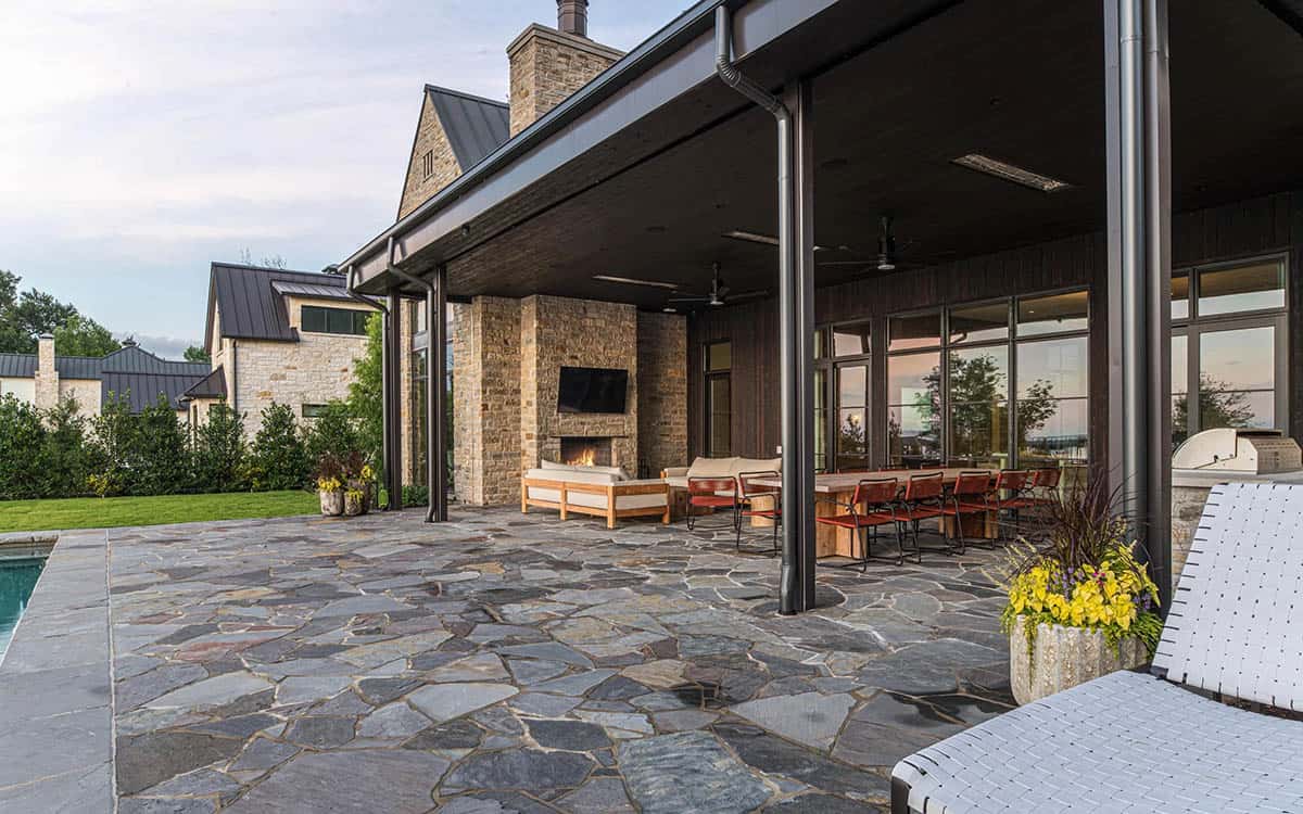 Covered patio with outdoor dining, lounge seating, and a stone fireplace beside a pool deck