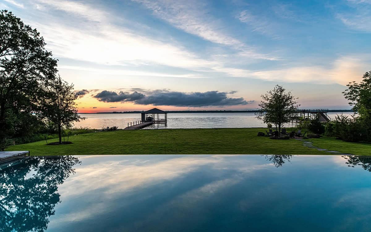 Panoramic sunset view over the lake from the pool's edge, with a boat dock and trees framing the scene