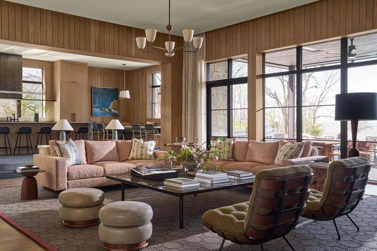 Living room with wood-paneled walls, blush sectional sofa, leather lounge chairs, and a view into the kitchen