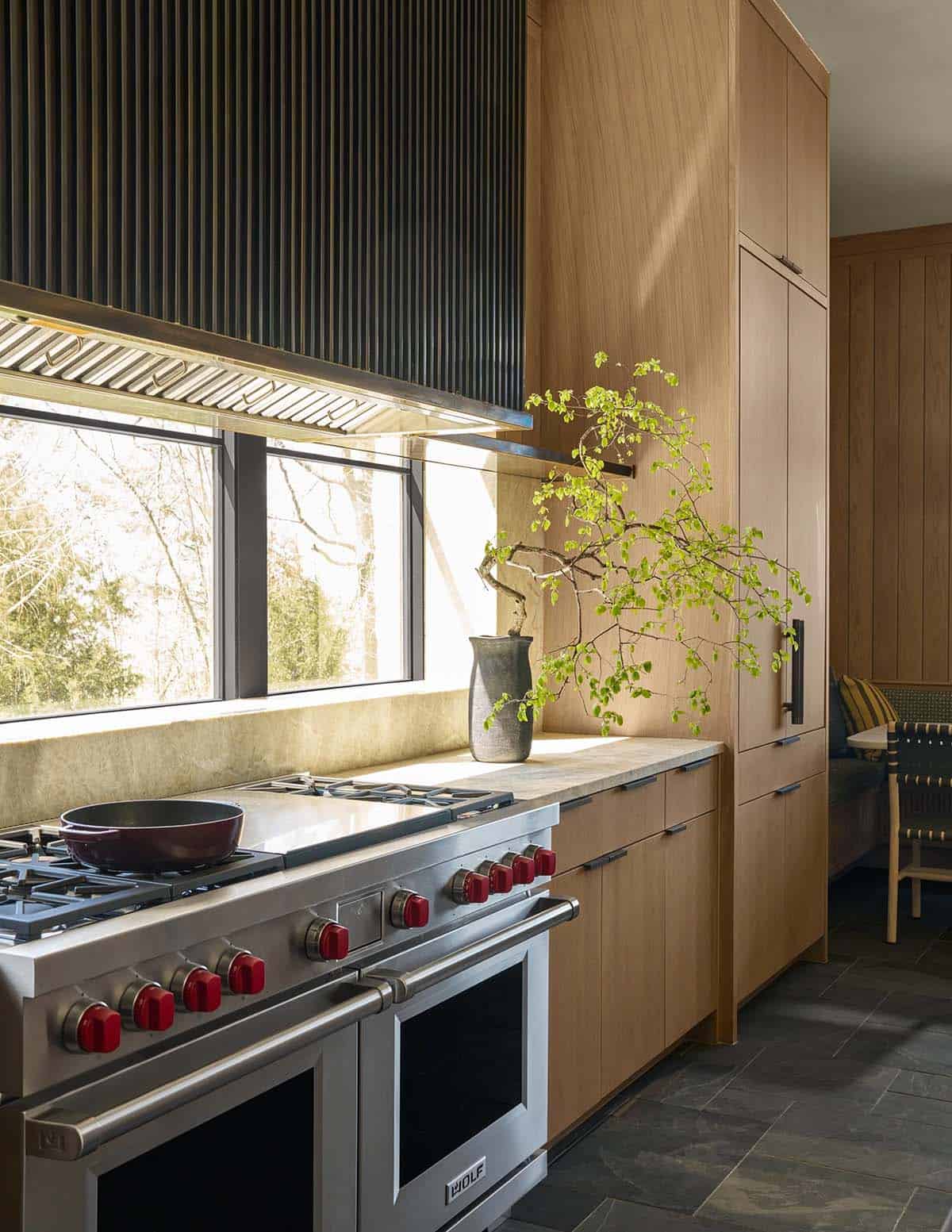 Close-up of a stainless steel range with red knobs beside wood cabinetry and a bonsai-style plant on the counter