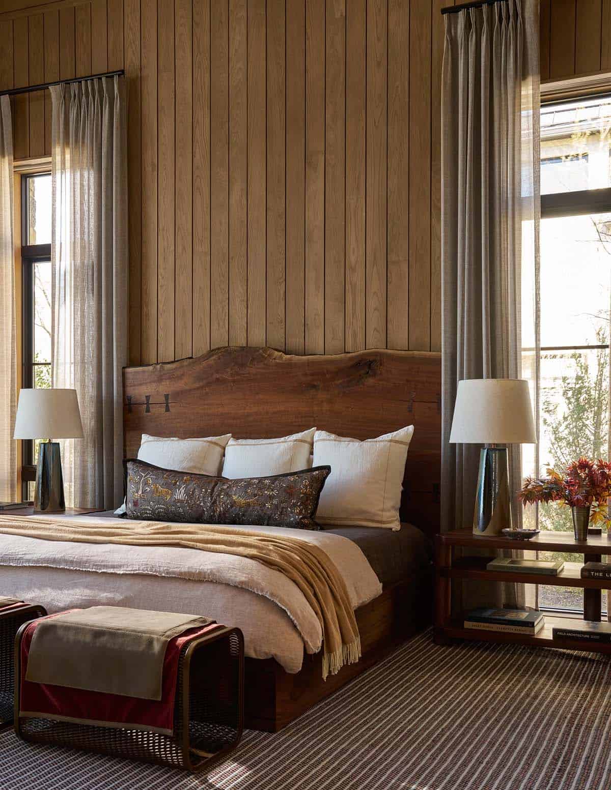 Bedroom with a live-edge wood headboard, wood-paneled walls, and linen drapery framing tall windows