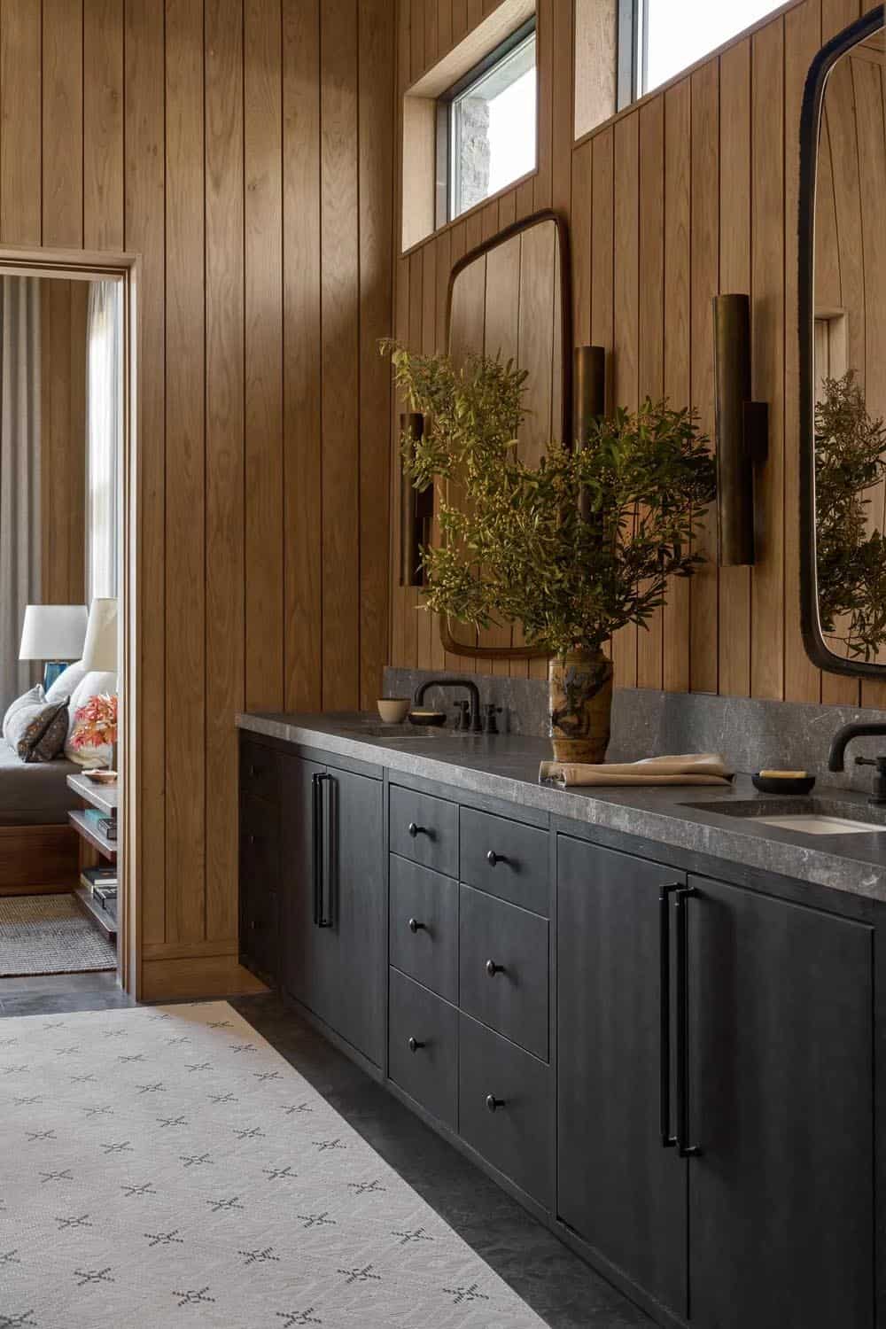 Bathroom with dark wood-toned vanity, stone countertop, brass sconces, and oak paneled walls