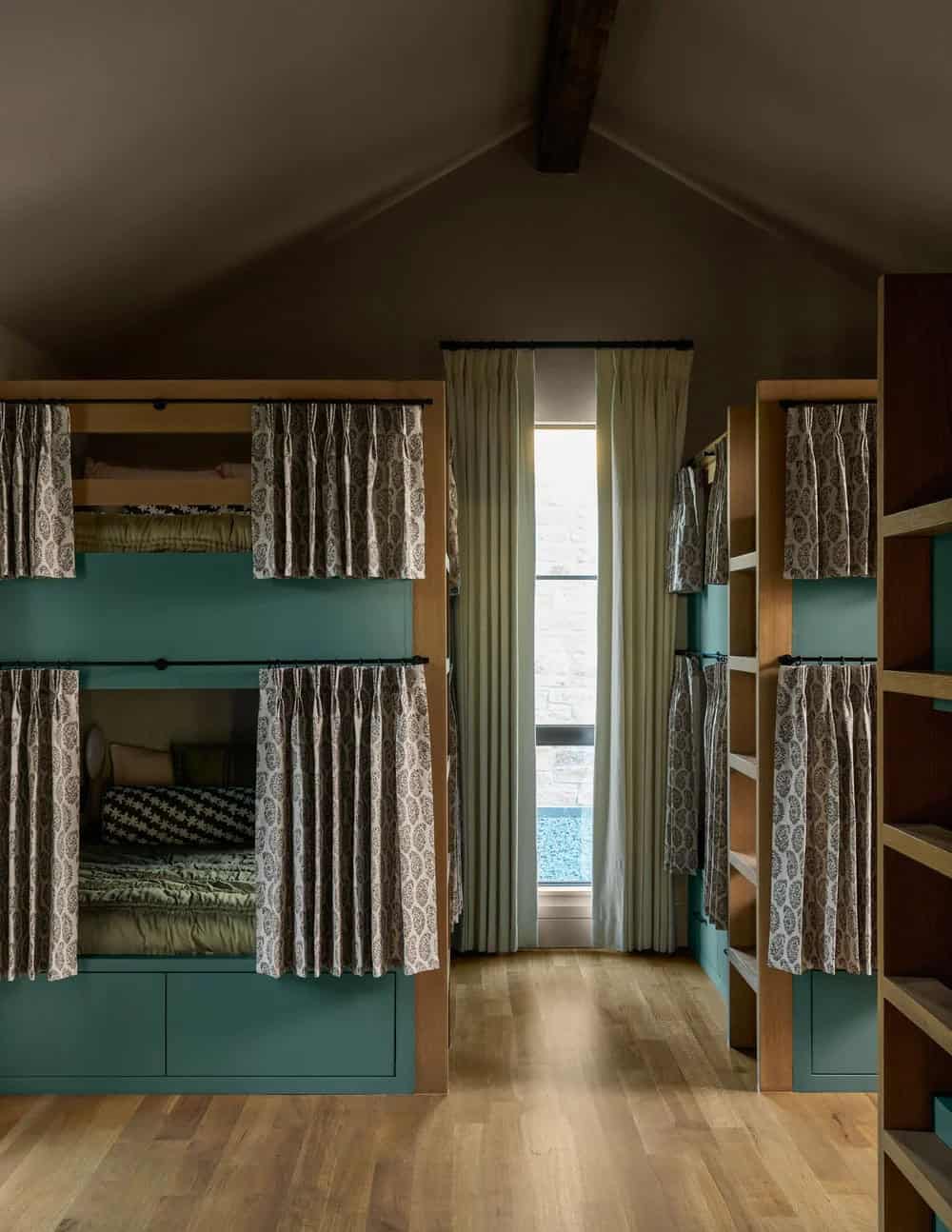 Built-in bunk room with teal cabinetry, patterned curtains for privacy, and a narrow window at the end of the hall
