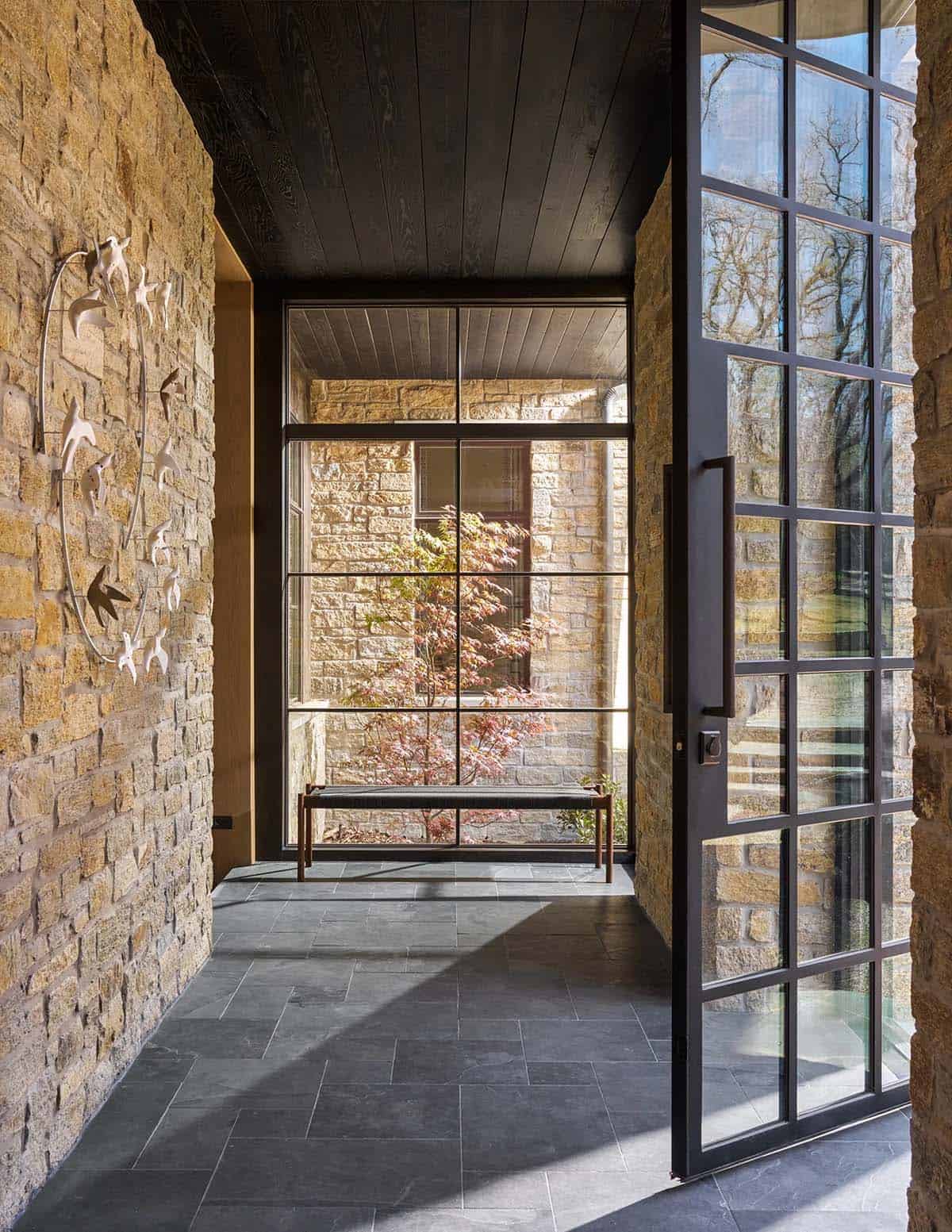 Entry hallway with stacked stone walls, slate flooring, a bird sculpture, and a glass door opening to a courtyard maple tree