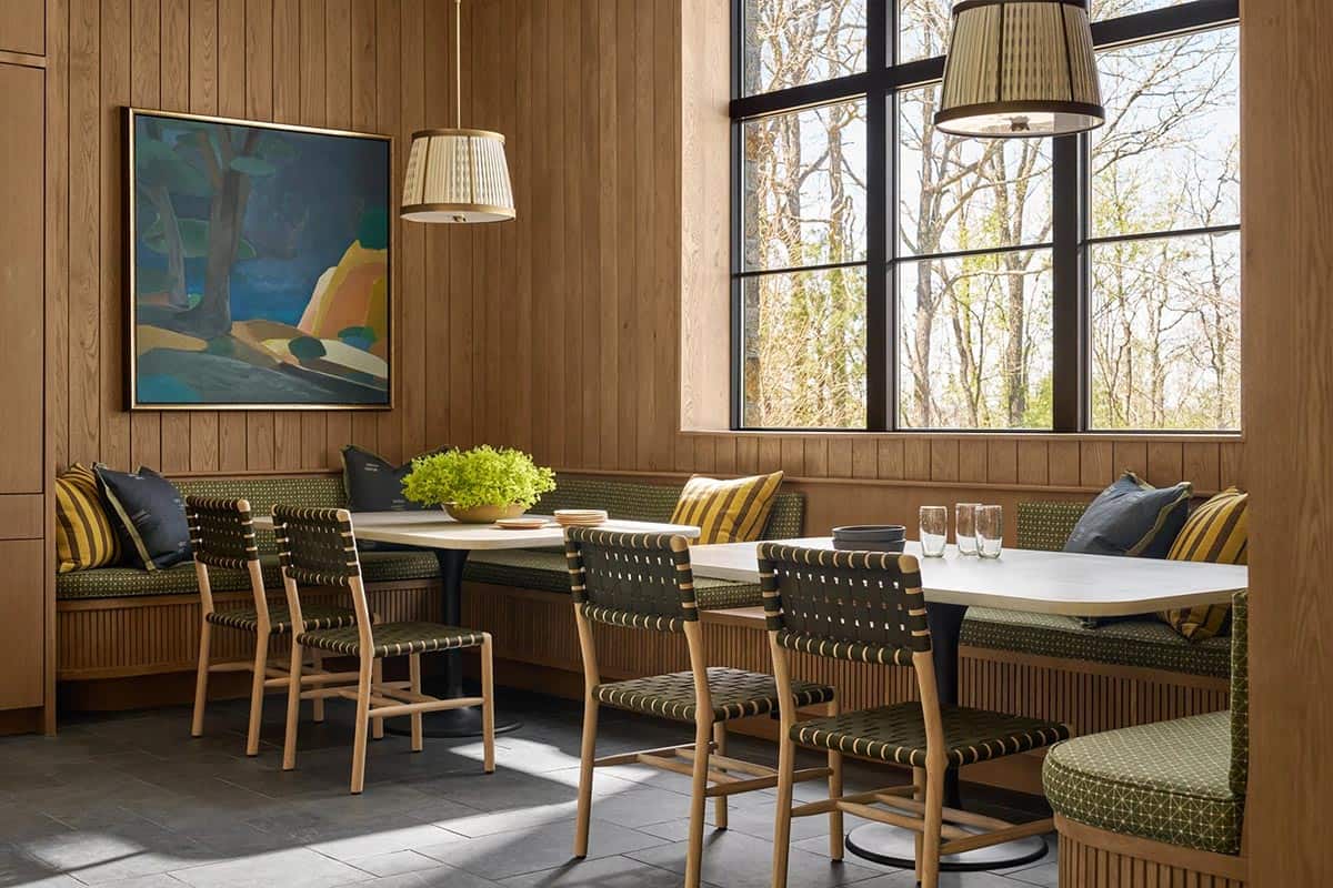 Breakfast nook with green banquette seating, striped pillows, a landscape painting, and pleated pendant lights
