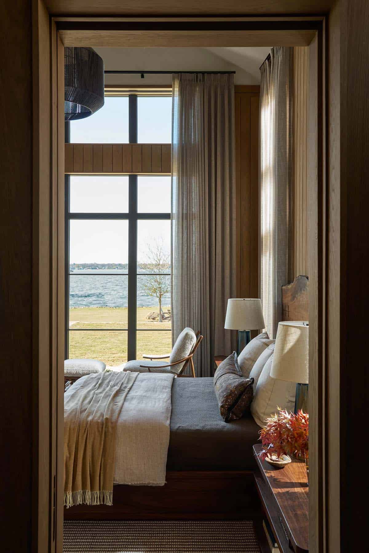 Bedroom doorway framing a bed with a live-edge headboard and floor-to-ceiling windows overlooking the lake