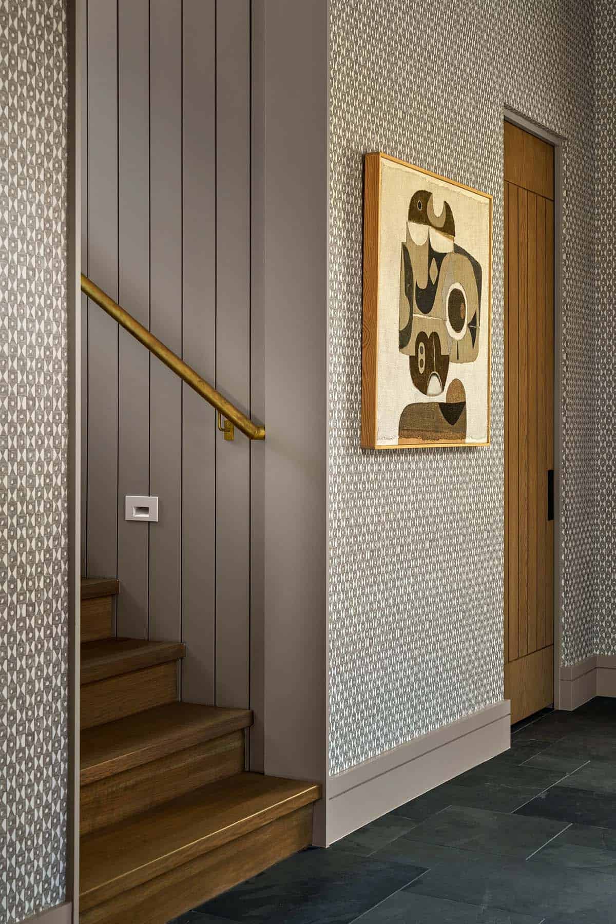 Stairway landing with patterned wallpaper, brass handrail, and an abstract framed artwork beside a wood door