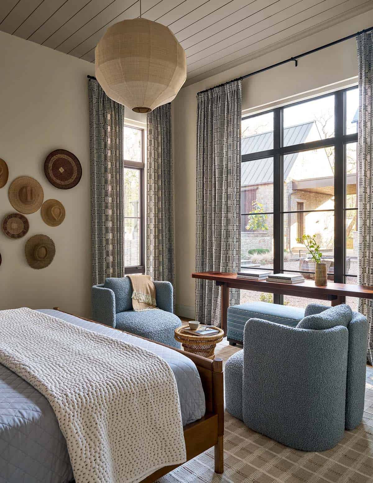 Bedroom with woven basket and hat wall display, blue boucl&eacute; chairs and ottomans, and a tall paper pendant light