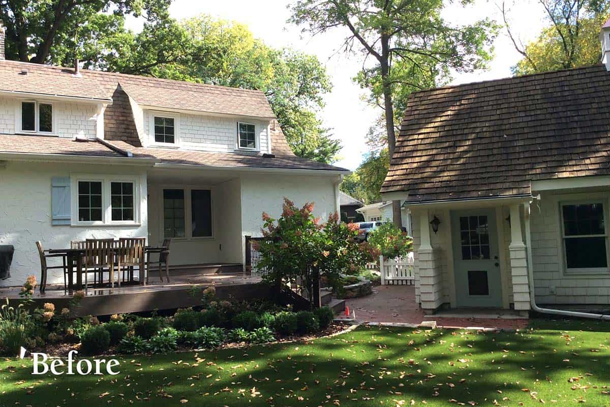 Before renovation: rear view of white cottage home with deck, original detached garage, and backyard garden beds