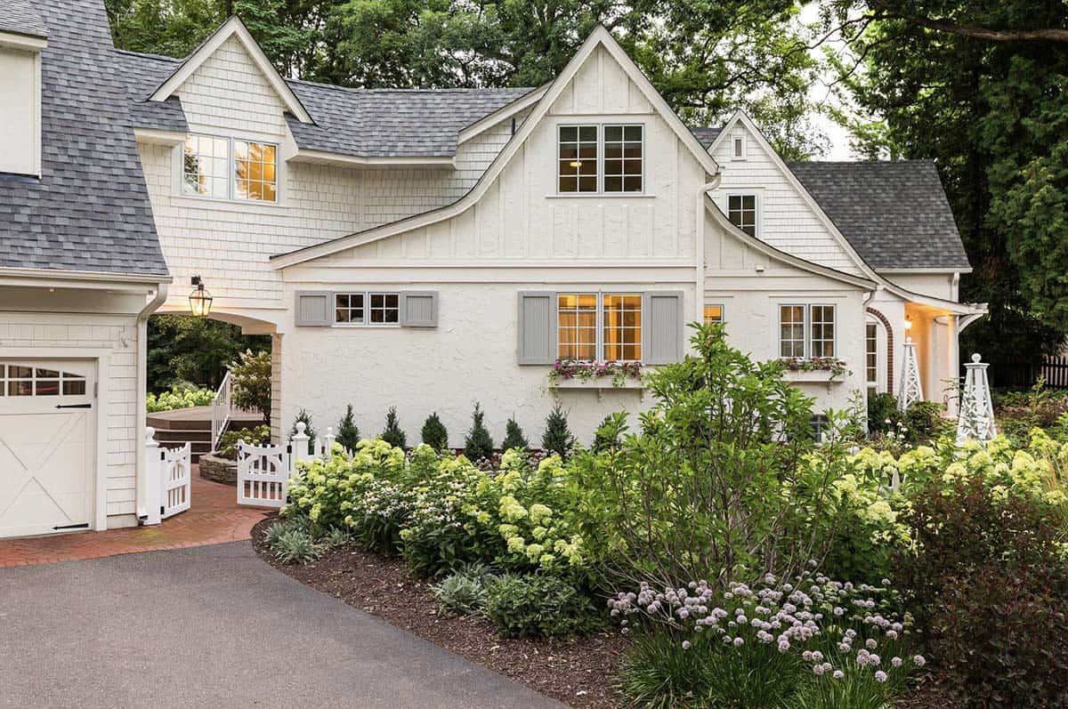 Side view of white cottage home with hydrangea borders and white garden gate at dusk