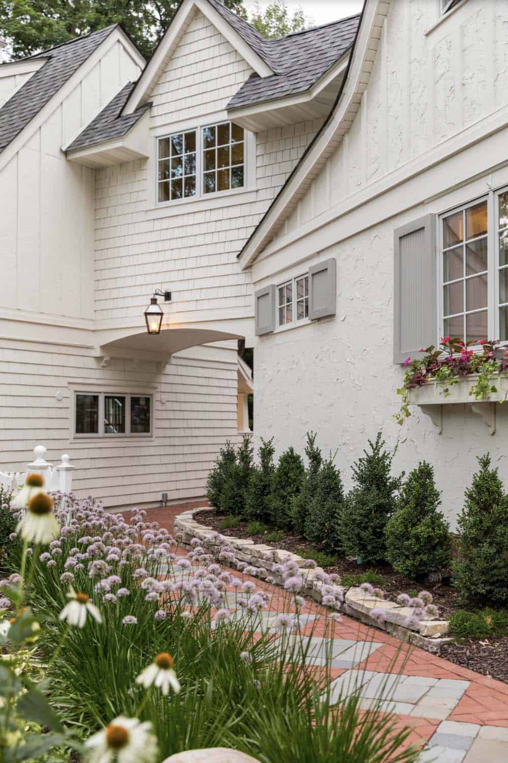 Brick pathway leading to white stucco home with gas lantern, allium blooms, and window boxes