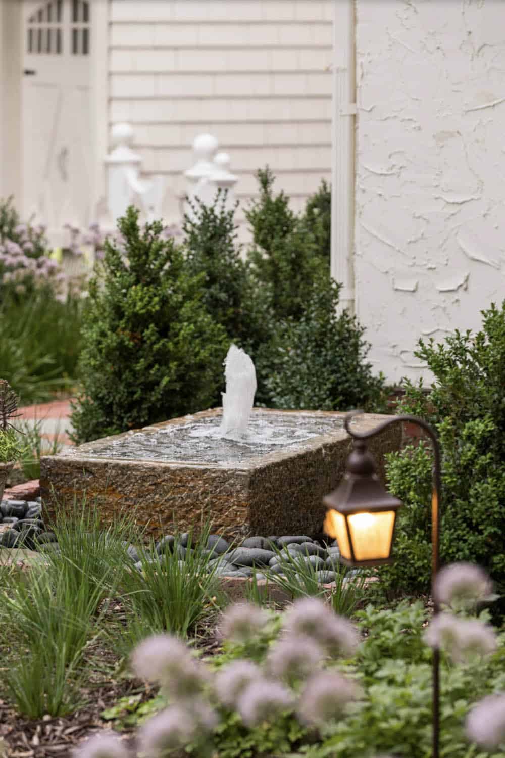 Close-up of granite block garden fountain with bronze path light and boxwood shrubs