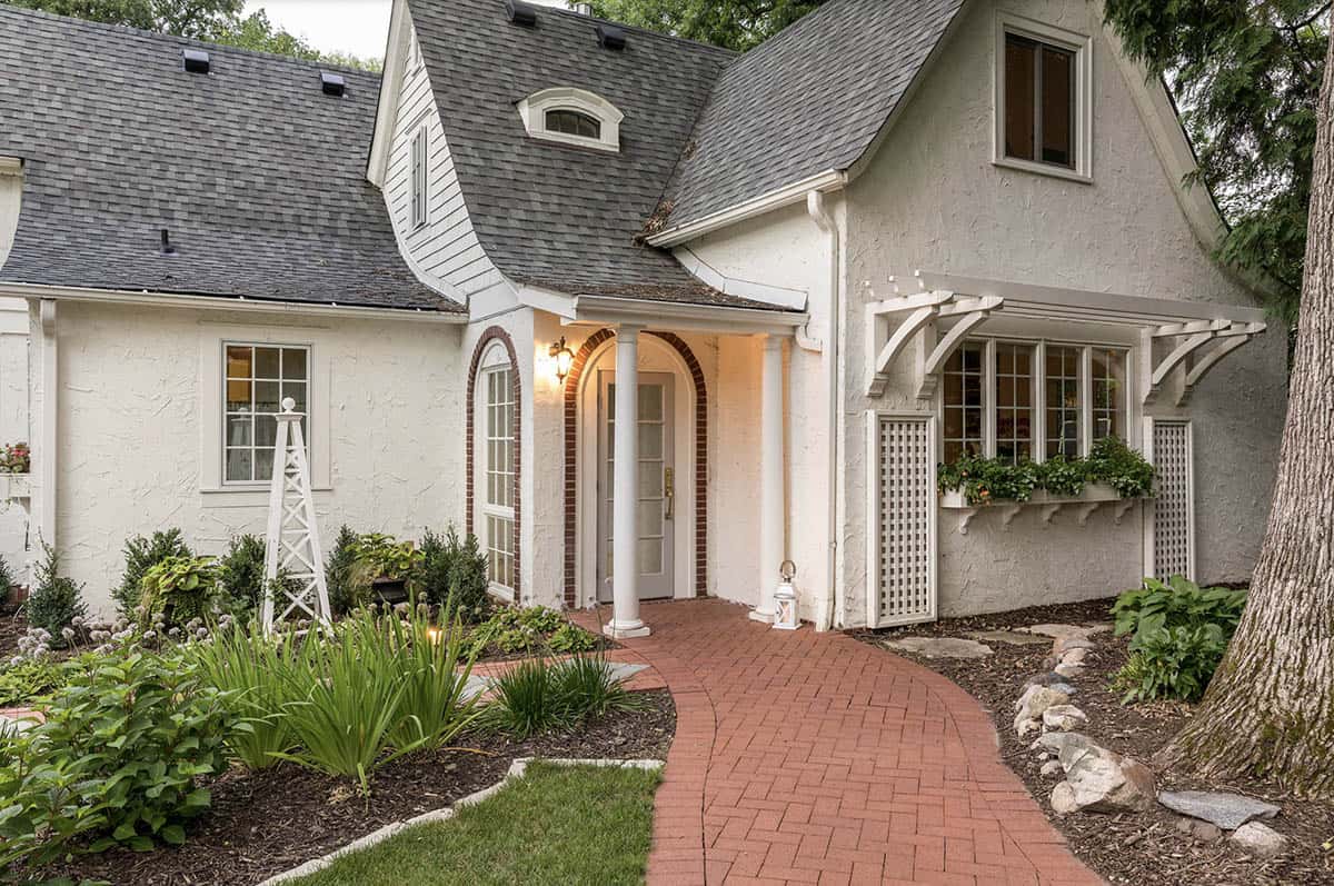 Brick front entry path leading to arched door with white columns, trellis, and window boxes