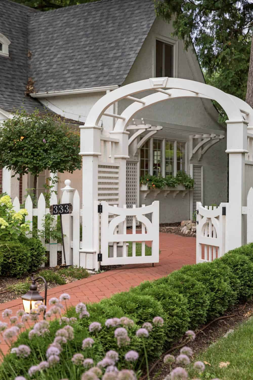 White arbor and decorative garden gate with allium flowers and brick pathway