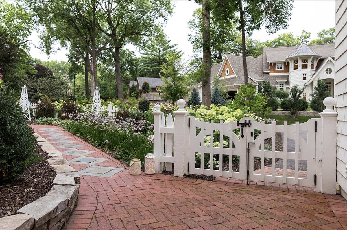 White garden gate opening to brick driveway courtyard with allium and hydrangea borders
