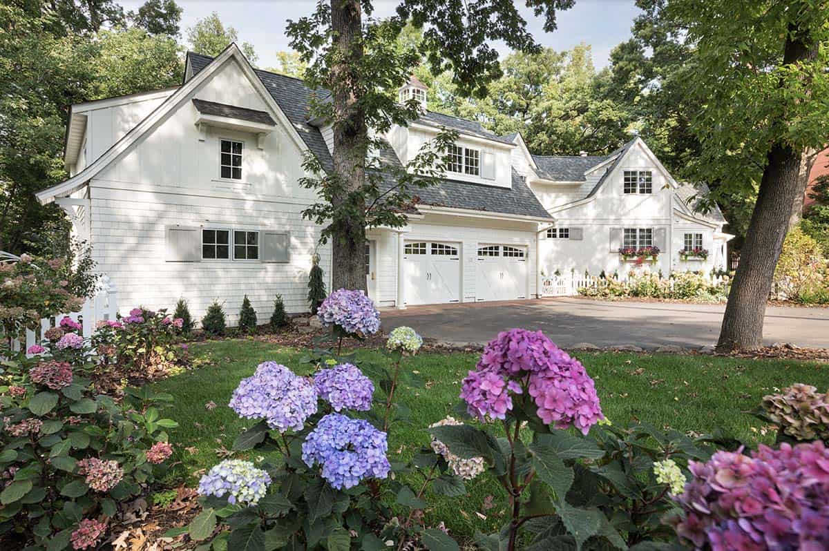 White cottage home with purple and pink hydrangeas in foreground, garage, and gray shuttered windows