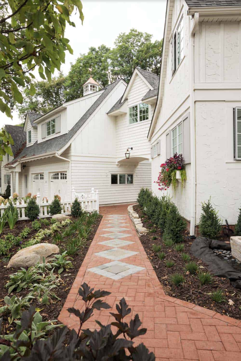 Brick and bluestone side path leading to white cottage home with copper cupola and colorful window boxes