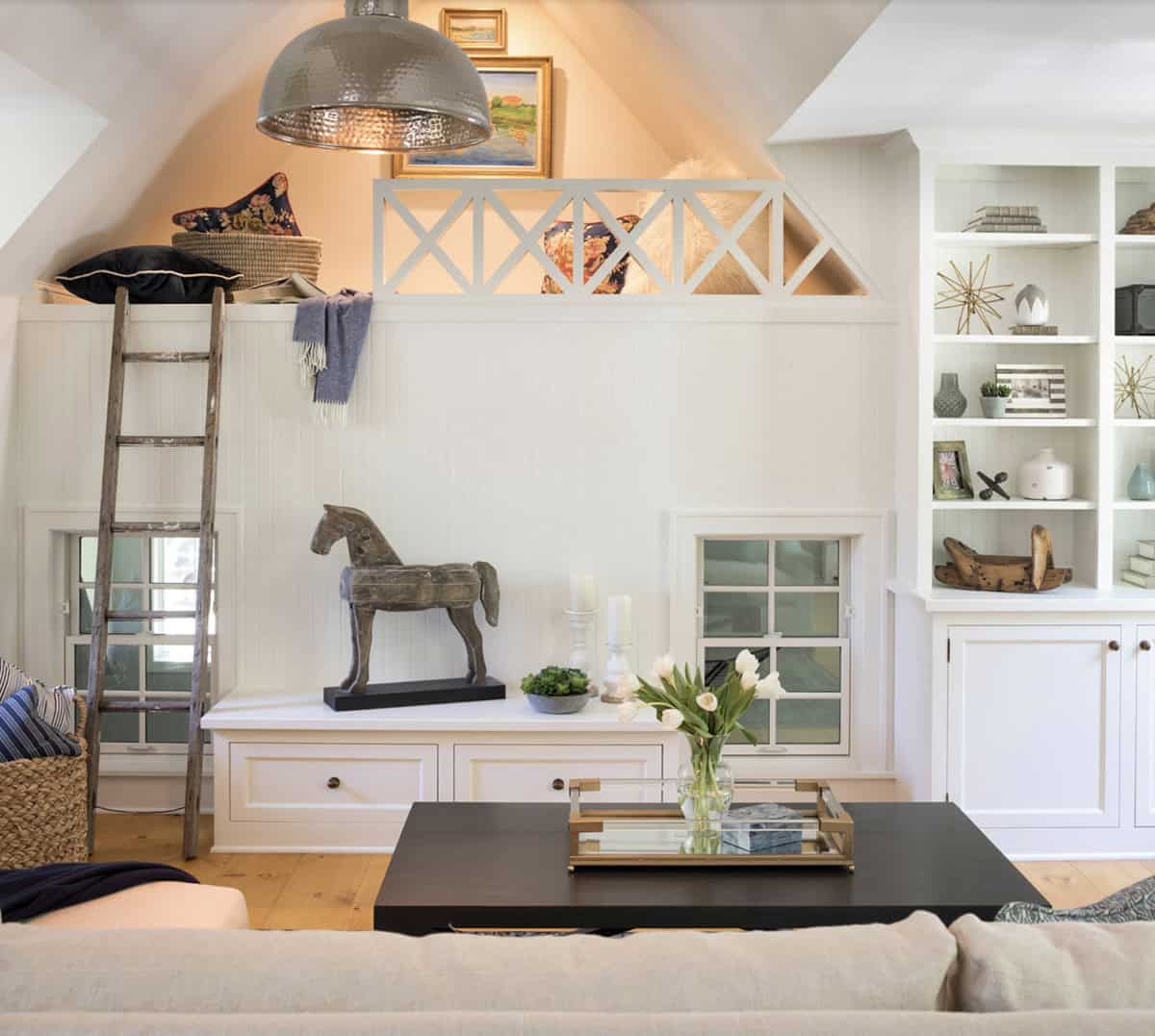 Carriage house living room with loft, ladder, built-in shelving, horse sculpture, and hammered pendant light