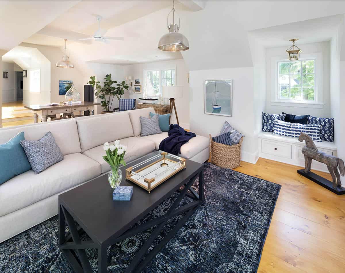Coastal-style carriage house living room with sectional sofa, navy rug, window seat, and sailboat artwork