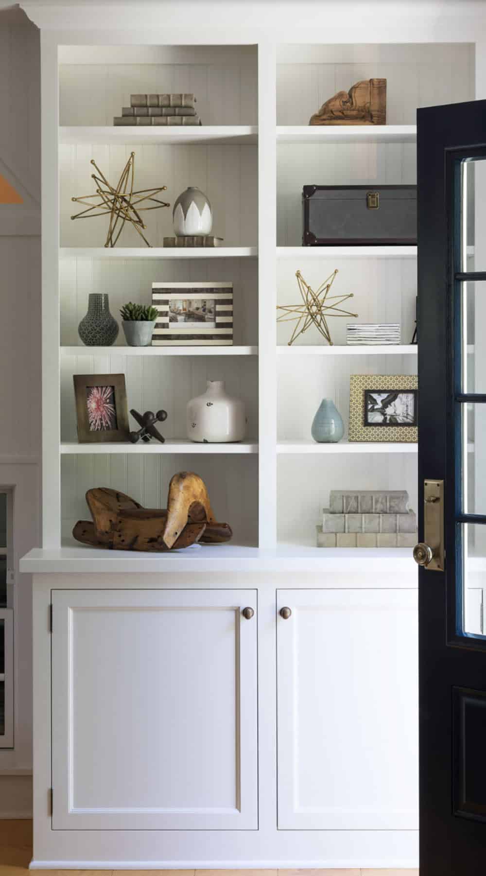 White built-in bookcase with coastal decor, gold star sculptures, ceramic vessels, and navy door