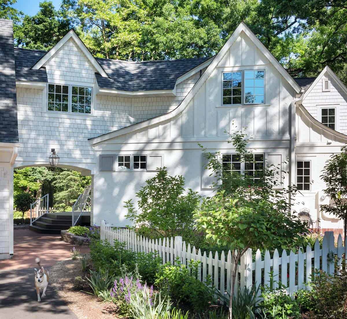 White cottage home addition exterior with husky dog, gas lantern archway, picket fence, and summer garden
