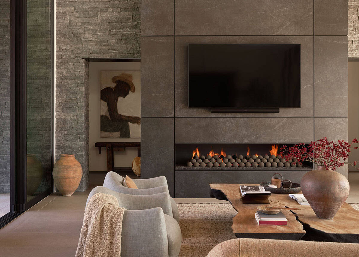 Living room fireplace wall clad in large-format stone tiles with linear gas insert, live-edge coffee table, and figurative artwork in adjacent niche