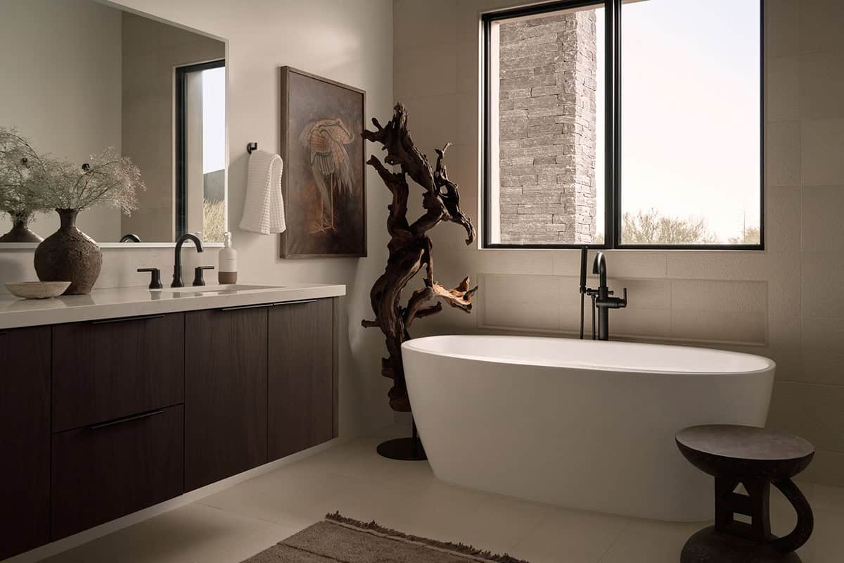 Guest bathroom with dark wood floating vanity, freestanding oval tub, driftwood sculpture, matte black fixtures, and stacked stone accent wall