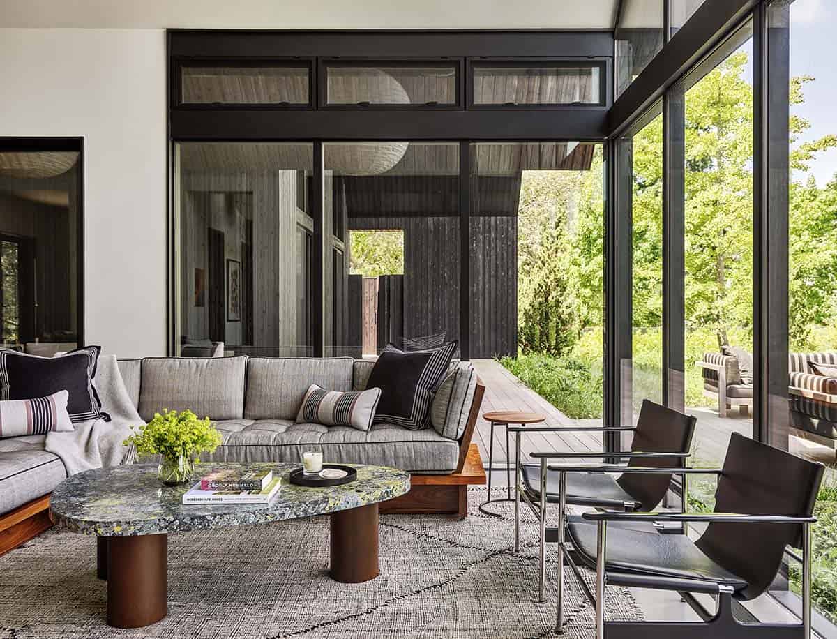 Living room with gray sectional sofa, stone coffee table, and glass walls opening to a deck