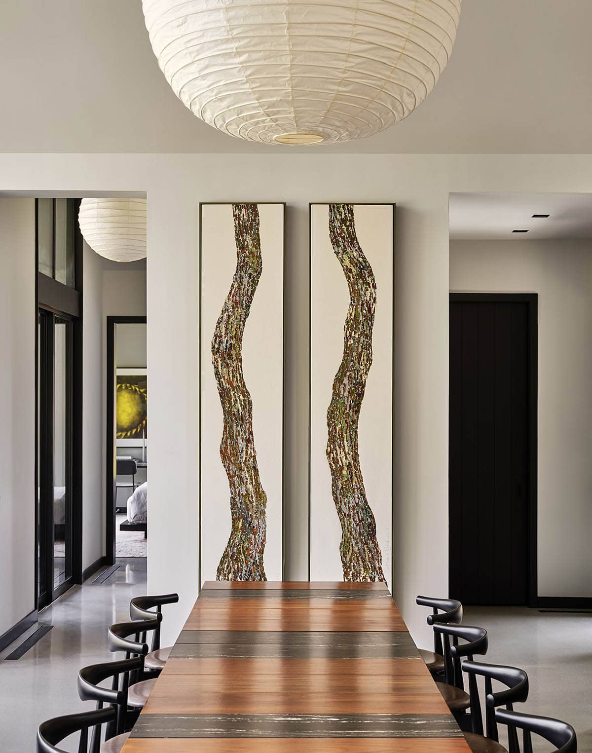 Dining room with long wood table and two tall abstract tree-bark paintings on the wall