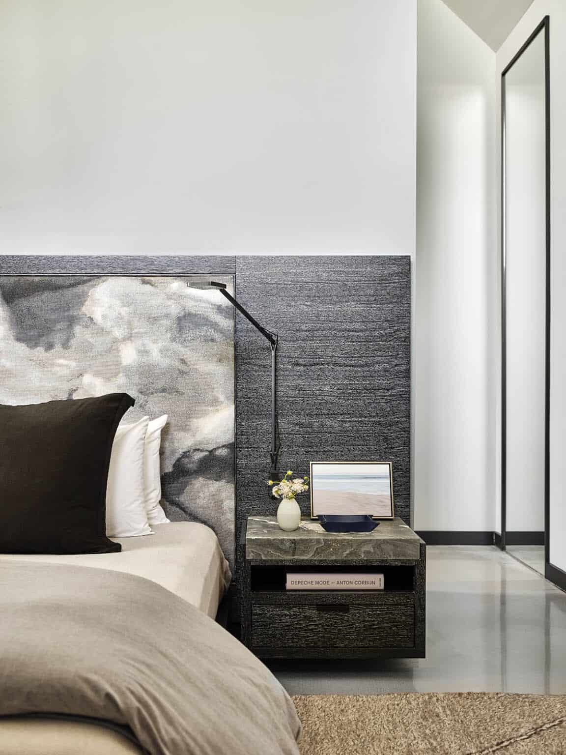 Close-up of a bedside table with marble top, wall-mounted reading light, and gray marble headboard