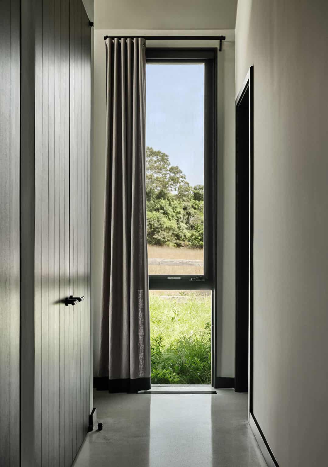 Narrow hallway with a tall curtained window overlooking a grassy meadow