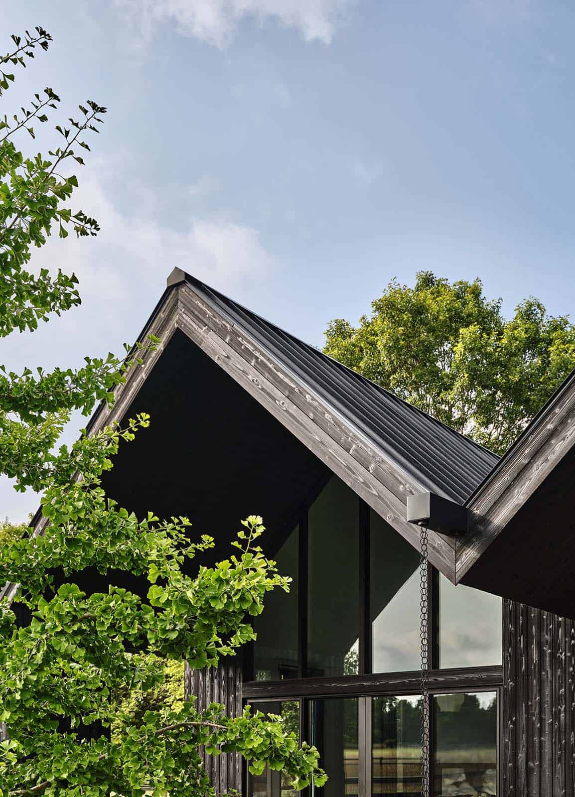 Close-up of a charred wood gable peak and standing-seam roof against blue sky and greenery