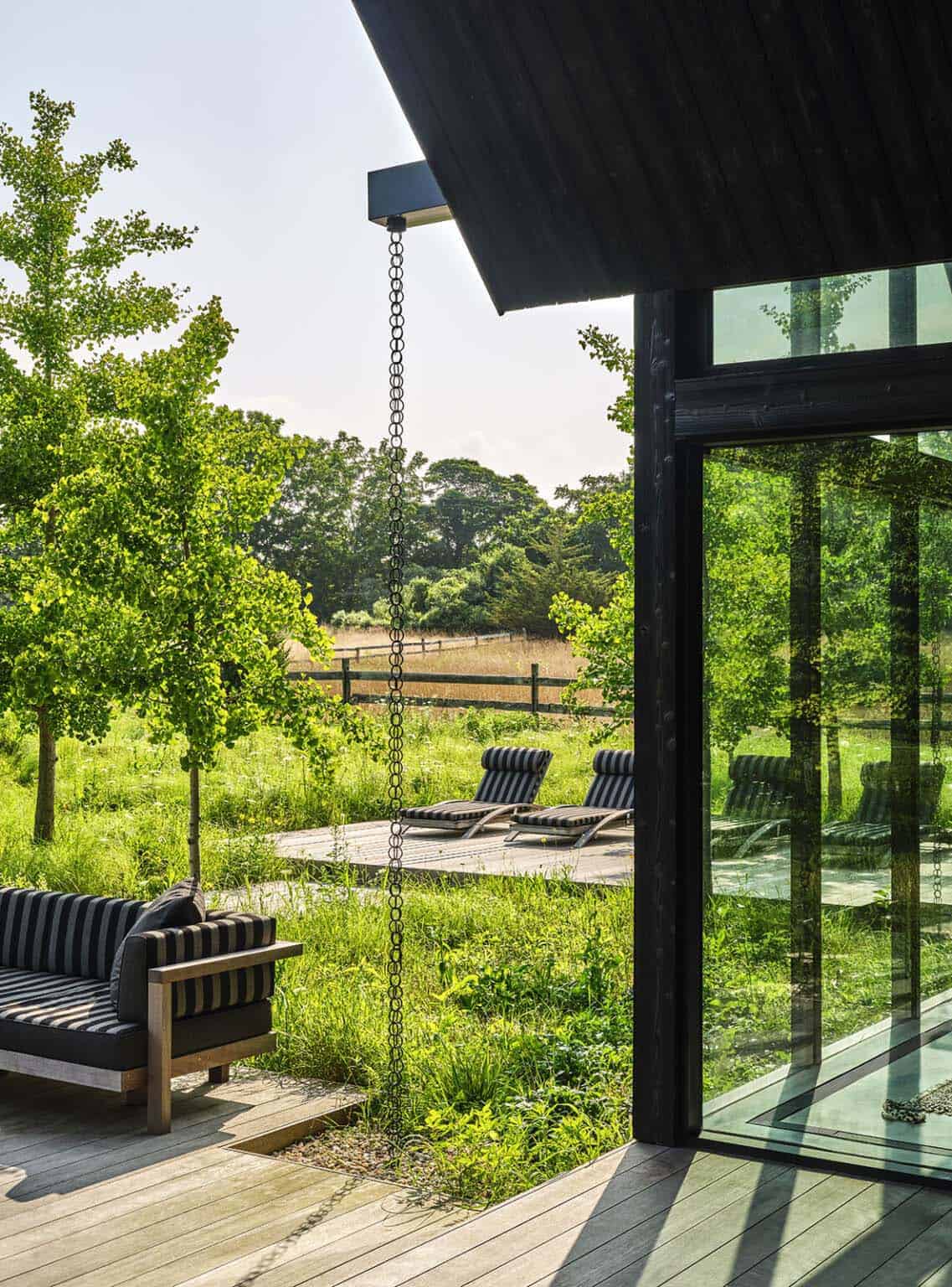 Striped outdoor lounge chairs on a deck beside a glass-walled pavilion overlooking a meadow