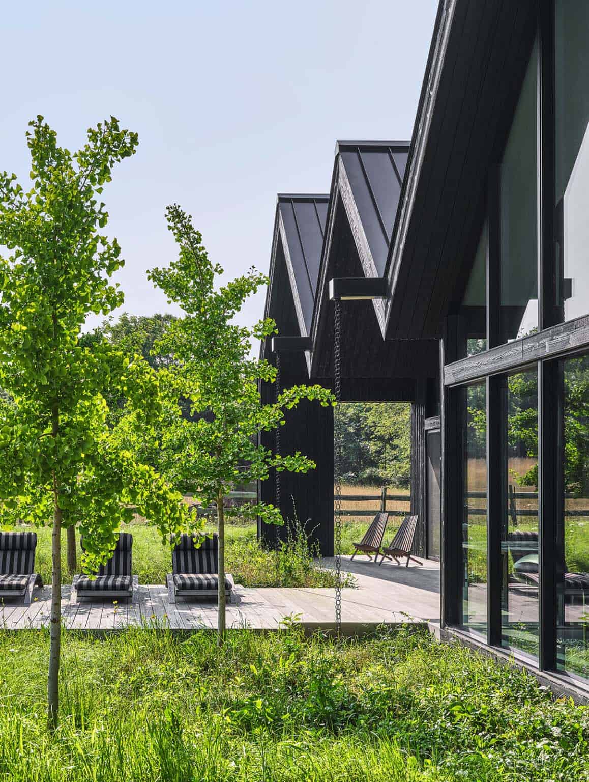 Exterior corner view of the gabled black house with striped lounge chairs and meadow fencing