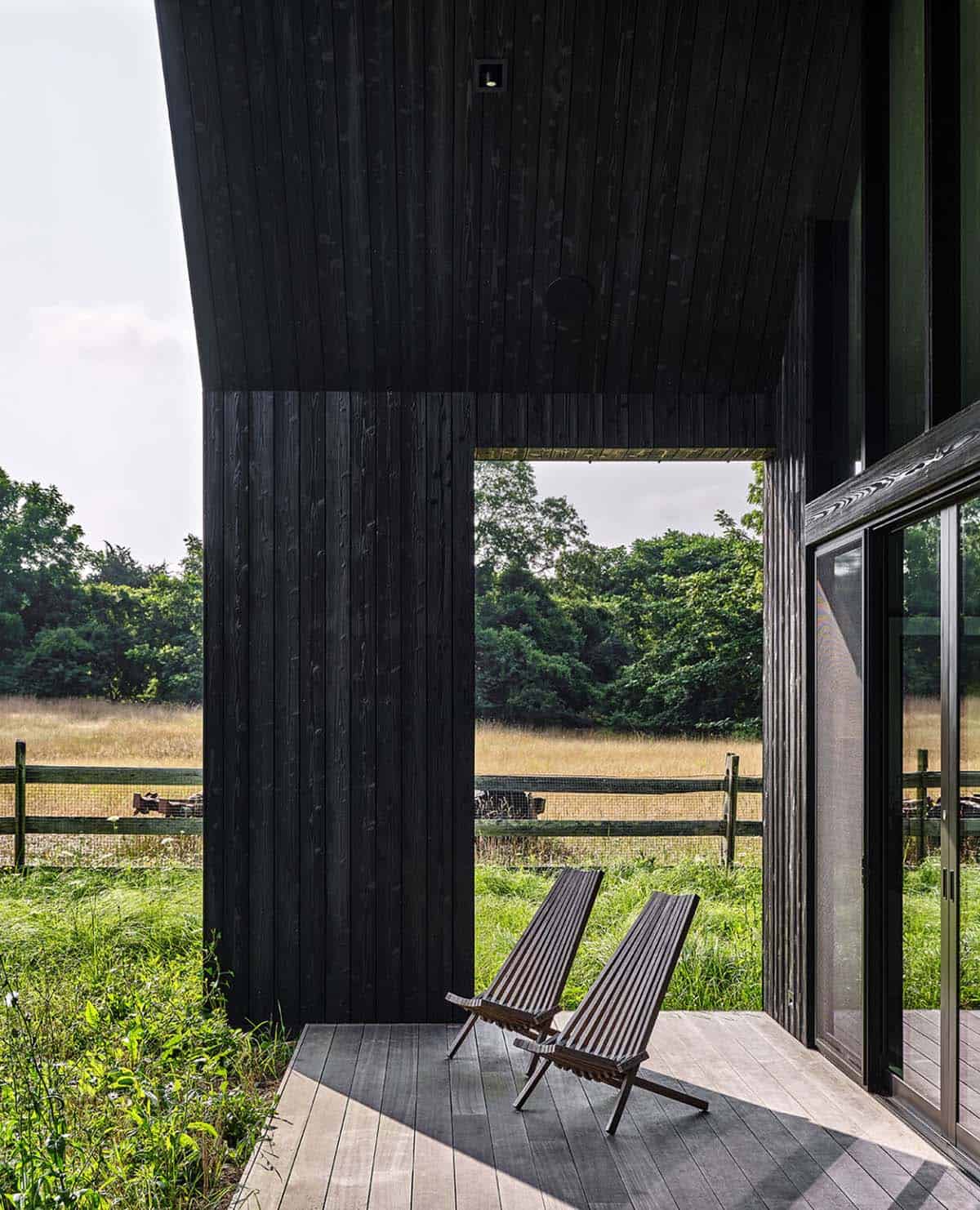 Covered deck corner with two wood lounge chairs framing a view of a fenced meadow