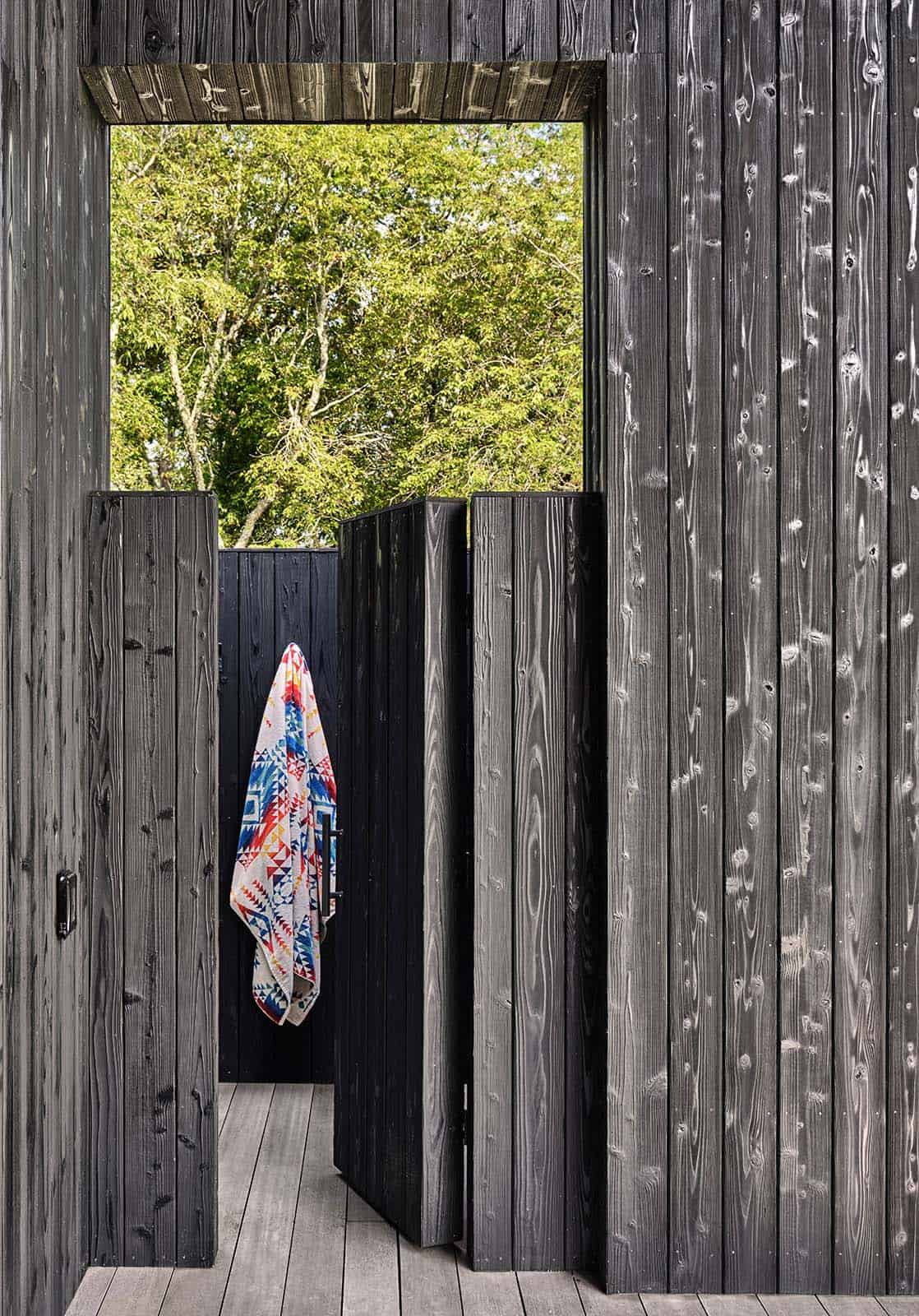 View through an open black wood door toward a hanging patterned towel and trees beyond