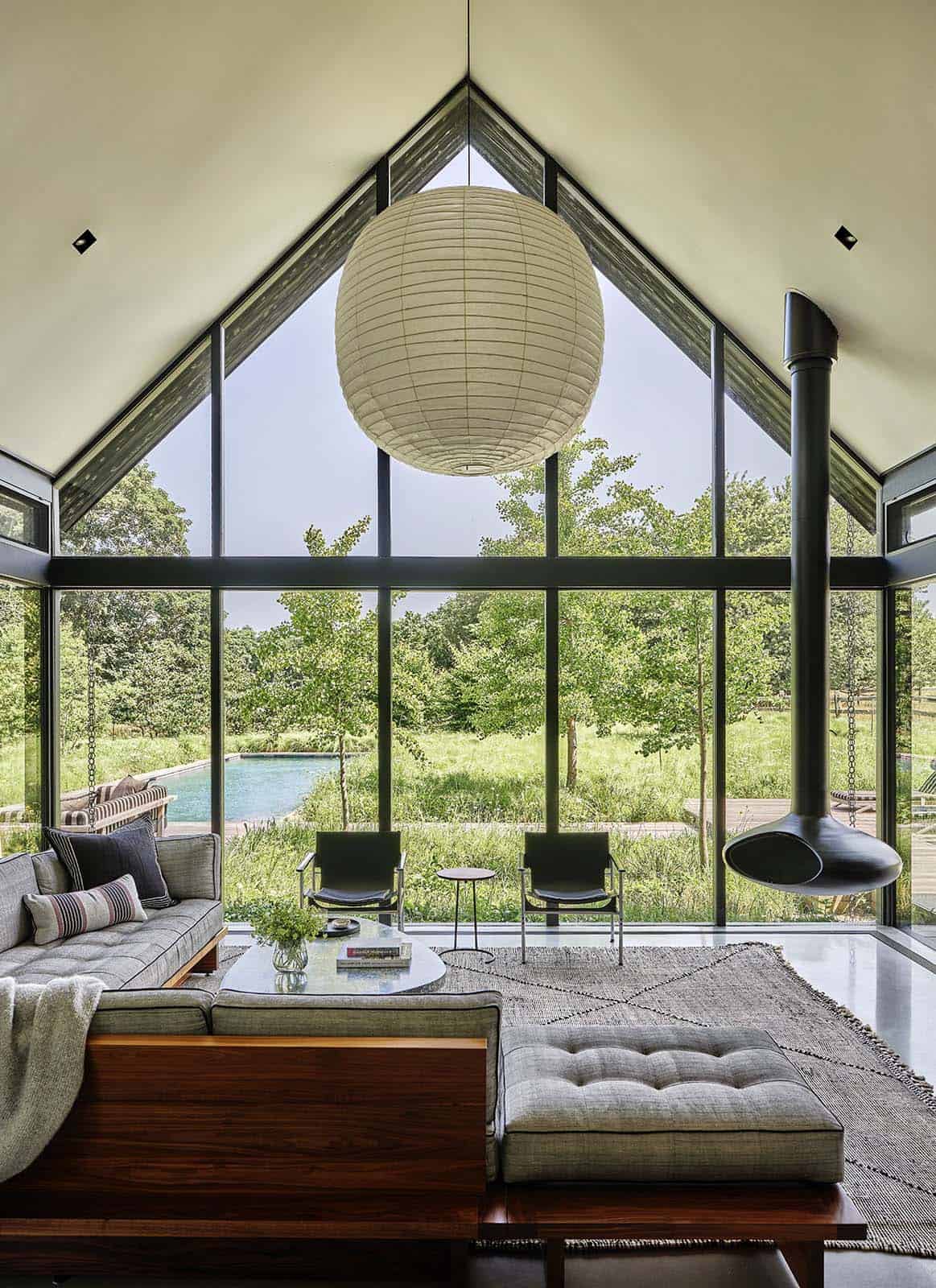 Vaulted living room with paper lantern pendant, hanging fireplace, and glass gable wall facing the pool
