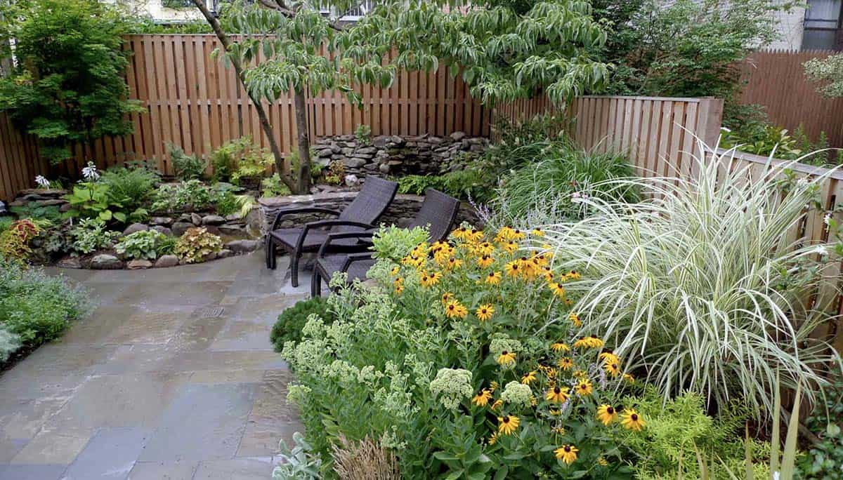 Flagstone patio with black-eyed Susans, ornamental grasses, and dry stone wall seating area in a small urban backyard