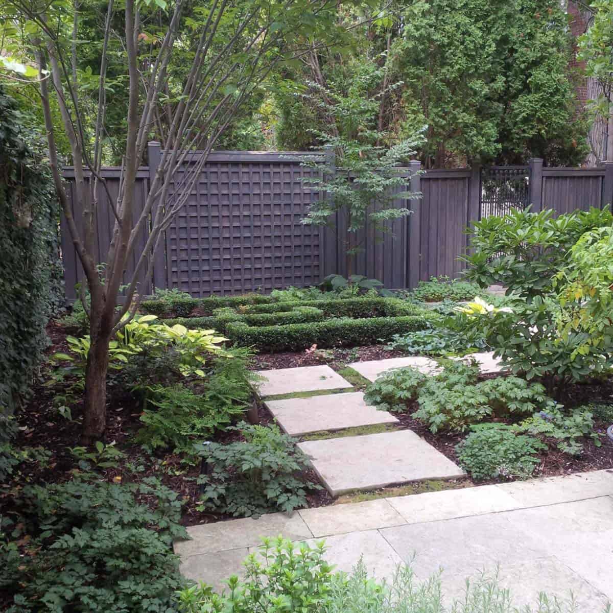 Flagstone stepping stone path with clipped boxwood parterres, hostas, and ferns in a shaded urban backyard