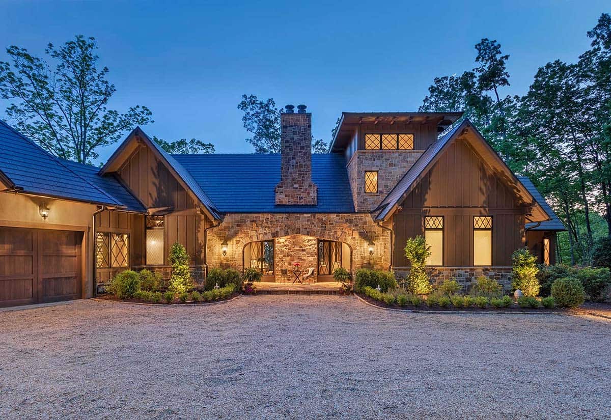 European-inspired lake house exterior at dusk with stone arch entry, board-and-batten siding, and metal roof