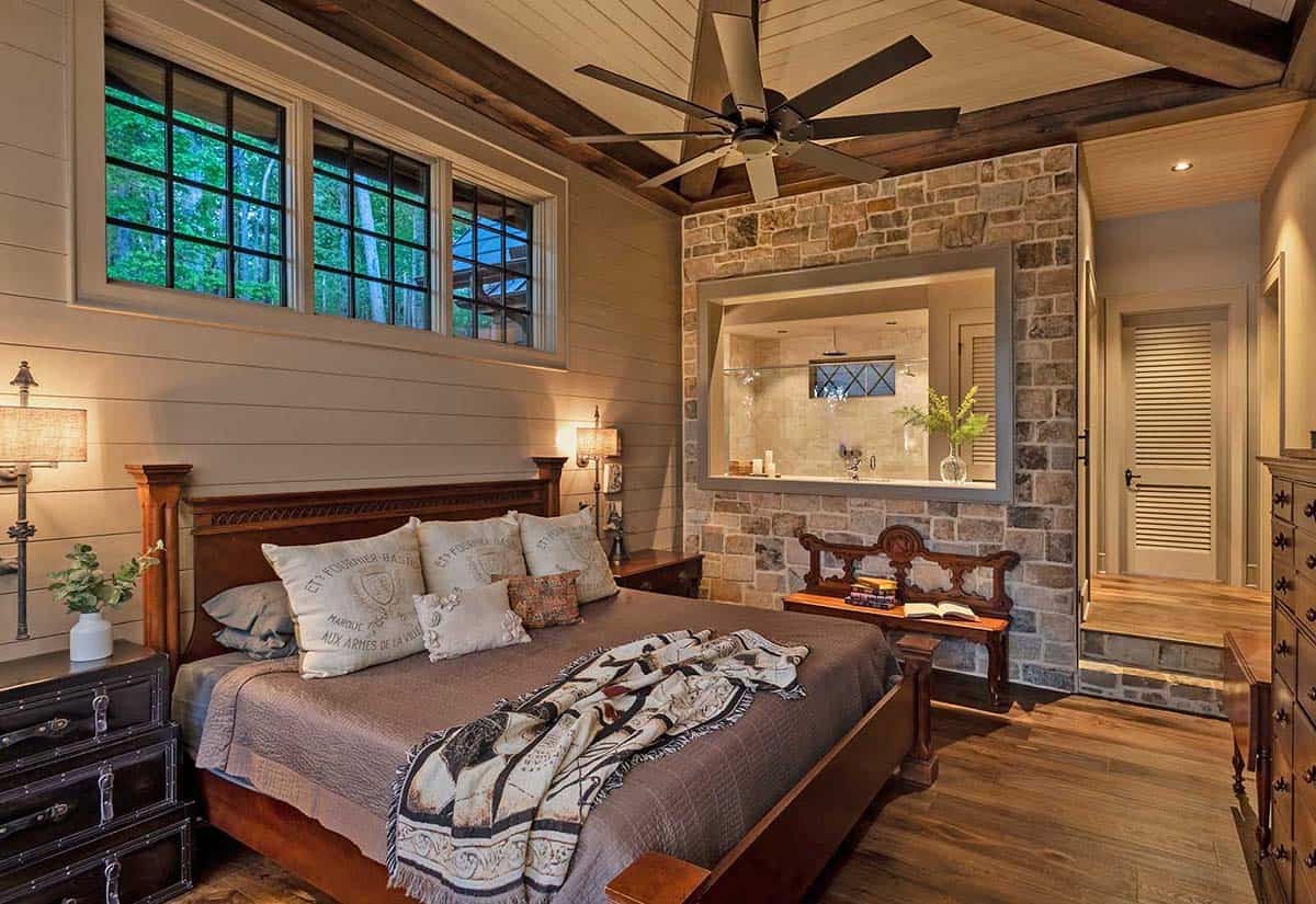 Primary bedroom with vaulted shiplap ceiling, exposed beams, stone accent wall, and pass-through bath window