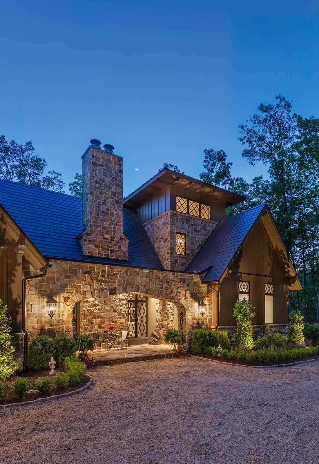 Lake house side exterior at twilight featuring stone chimney, arched entry, and diamond-pane windows