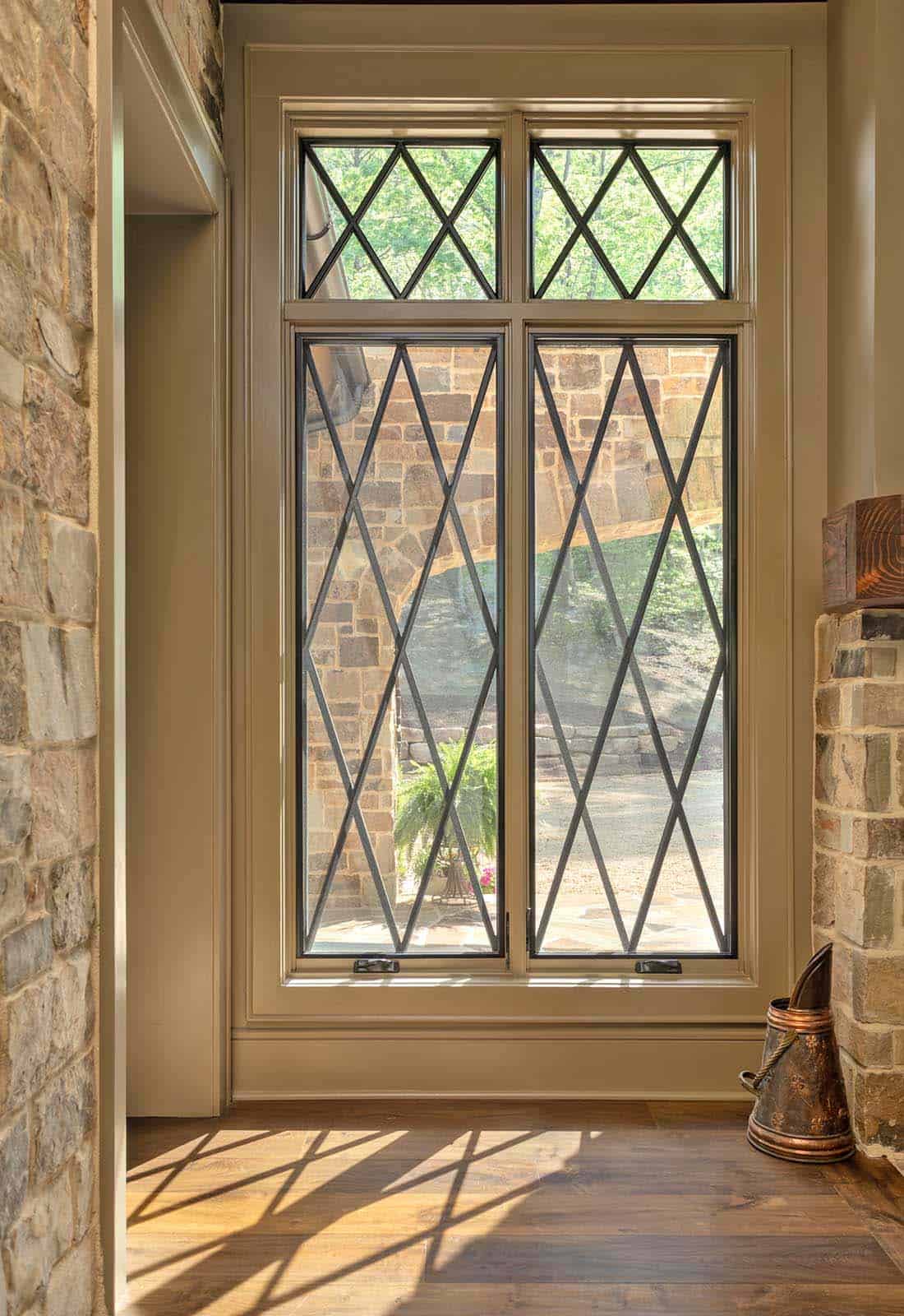 Diamond-pattern casement windows casting geometric shadows on hardwood floors beside a stone fireplace